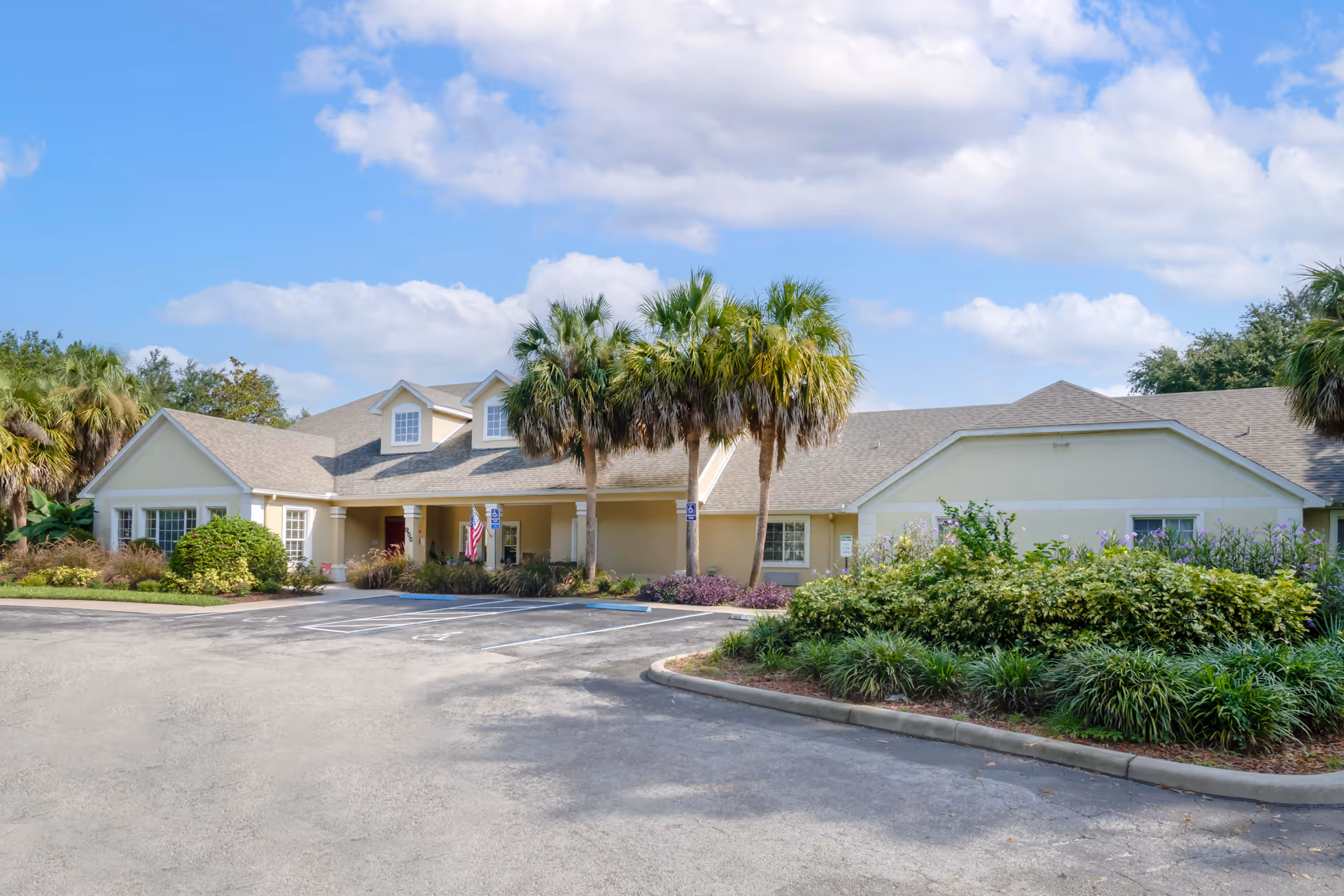 Front exterior of a single-story Brookdale Port Orange building with palm trees, landscaped beds, and a parking area under a blue sky.