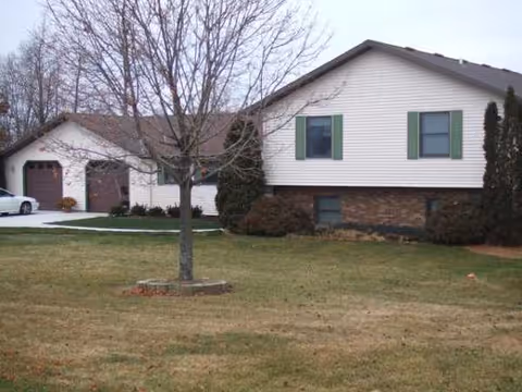 Two-story suburban-style building with a front lawn, leafless tree, and attached garage.