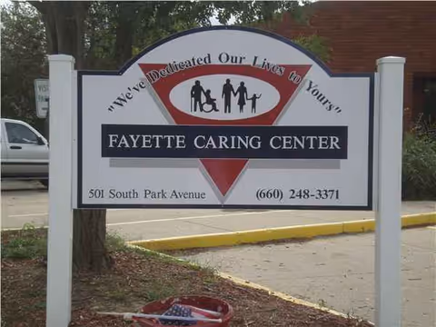 Outdoor sign for Fayette Caring Center with address and phone, set against a brick building.