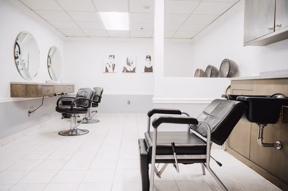 A clean salon room with black styling chairs, round mirrors, and wash sinks in a bright interior.