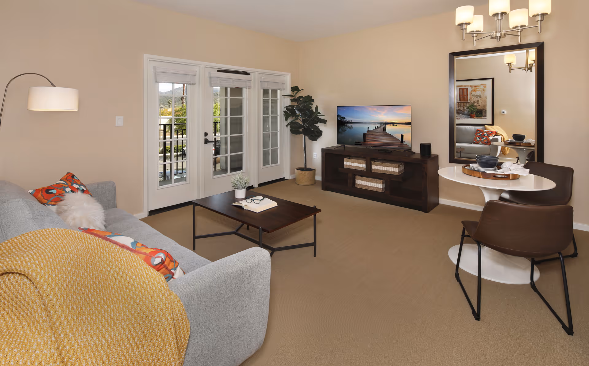 Well-lit living room with a sofa, coffee table, TV on a stand, round dining table and French doors to a balcony.