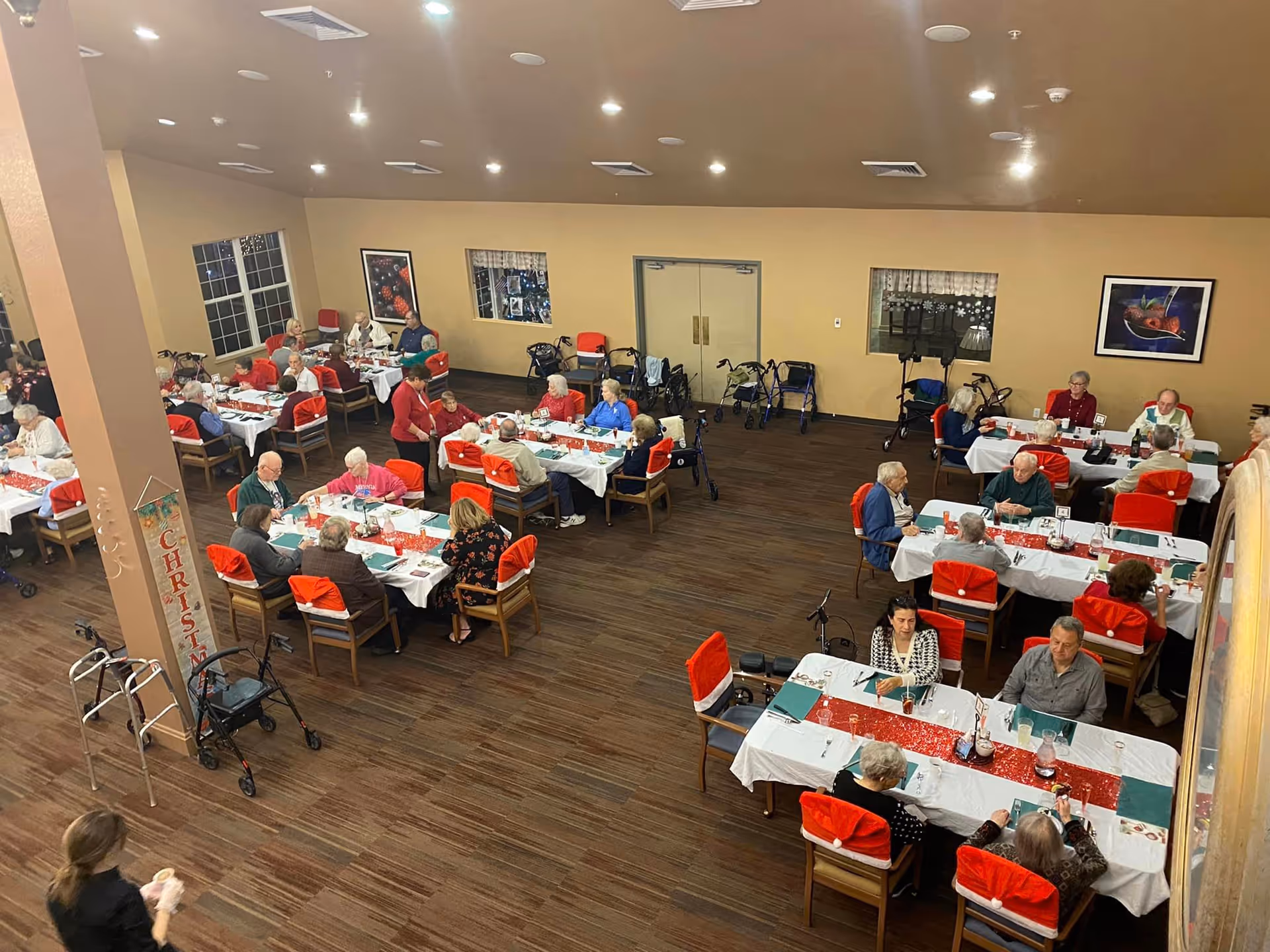 A large dining room with seniors seated at holiday-decorated tables for a communal meal.