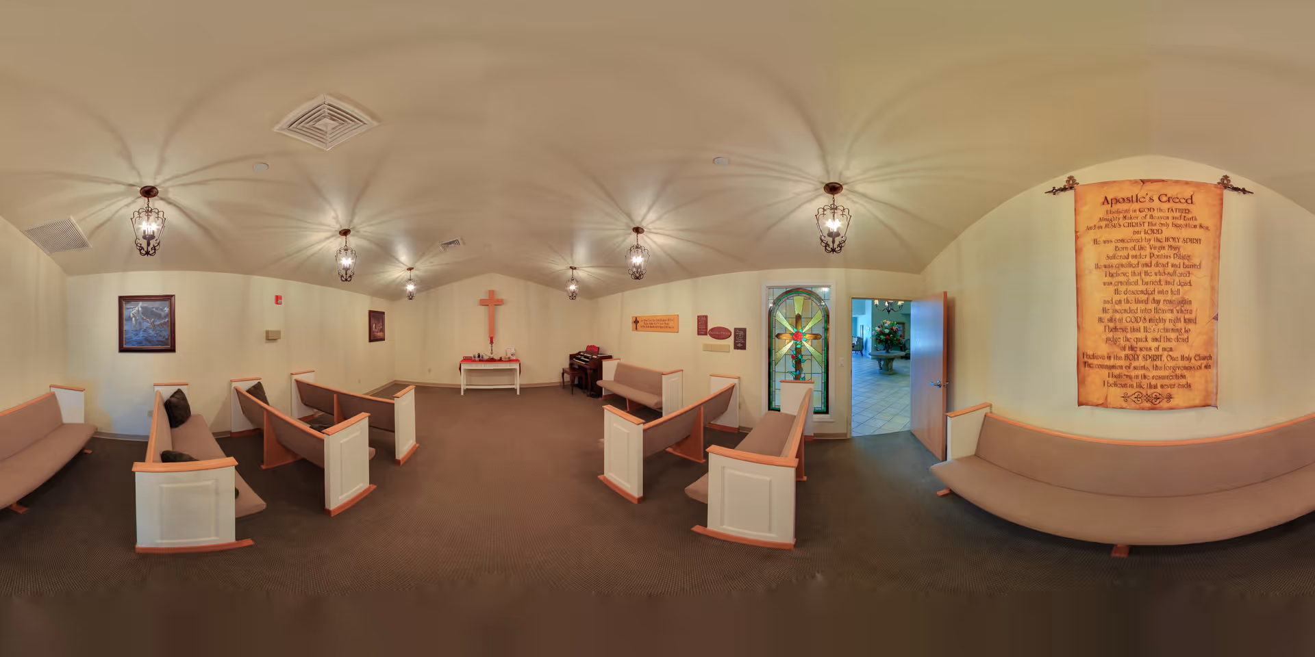 Small chapel-style room with pews facing a cross and altar, a stained-glass doorway, and a framed creed on the wall.