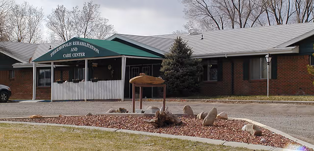 Front exterior of a one-story brick rehabilitation and care center with a green entrance awning and a circular landscaped bed.