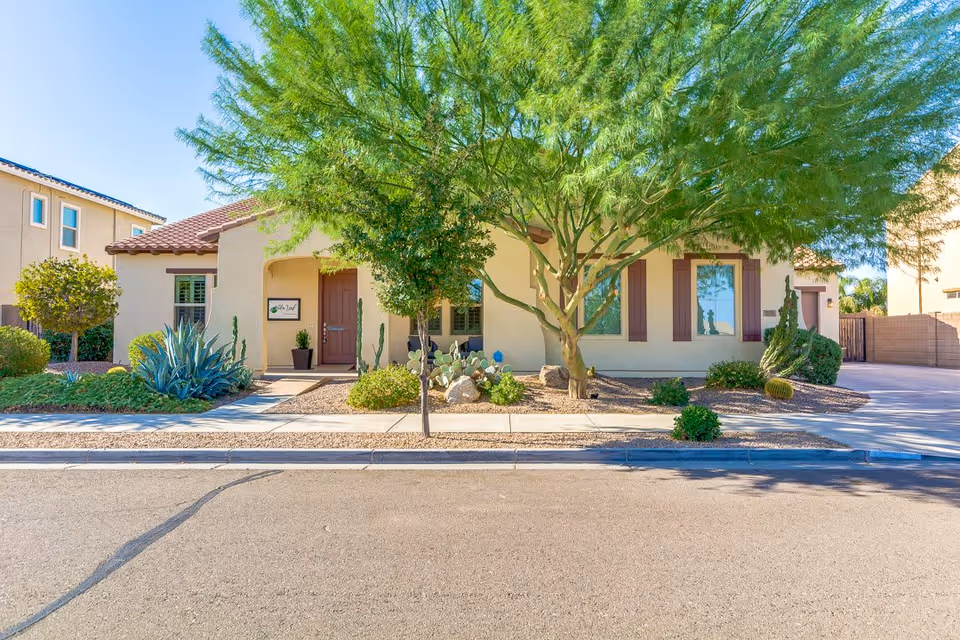 Front exterior of a single-story beige building with a large tree, desert landscaping, and a visible entrance sign for Alder Leaf.