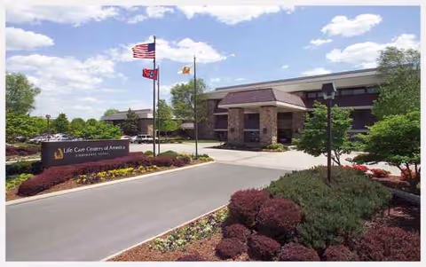 Front exterior of Life Care Centers of America building with flagpoles and landscaped entrance.