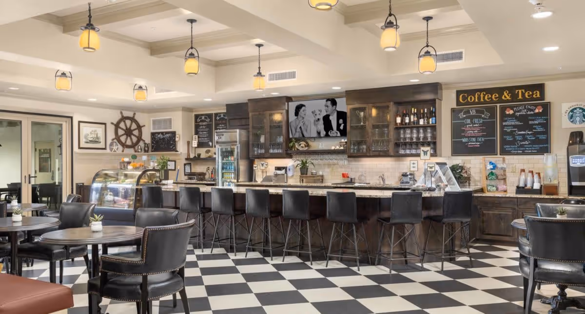 A bright café-style dining area with a long service counter, barstools, round tables and a 'Coffee & Tea' menu board.