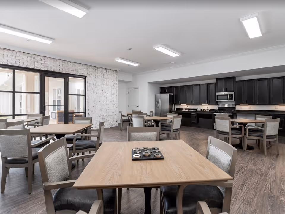 Spacious communal dining area with multiple tables and chairs and a full kitchen with dark cabinets along the back wall.