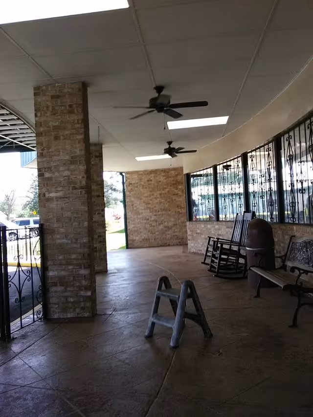 Covered front porch with brick pillars, ceiling fans, rocking chairs and benches at a senior living facility.