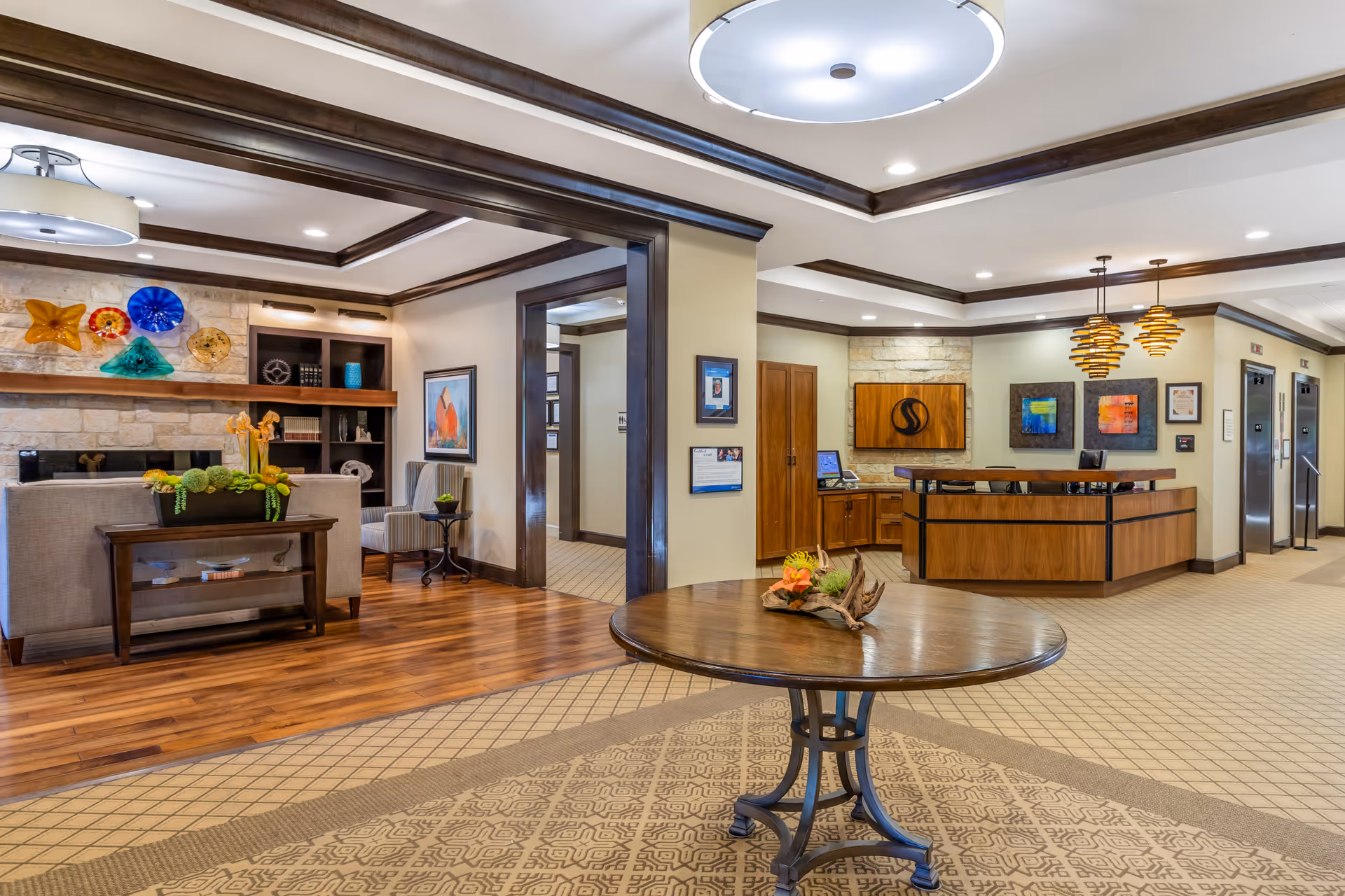 Sunlit interior lobby with a round table in the foreground, a seating area to the left and a reception desk to the right.