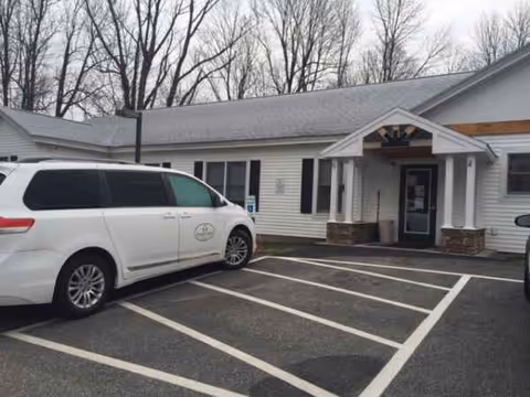 White single-story senior living facility entrance with a parked white van nearby.