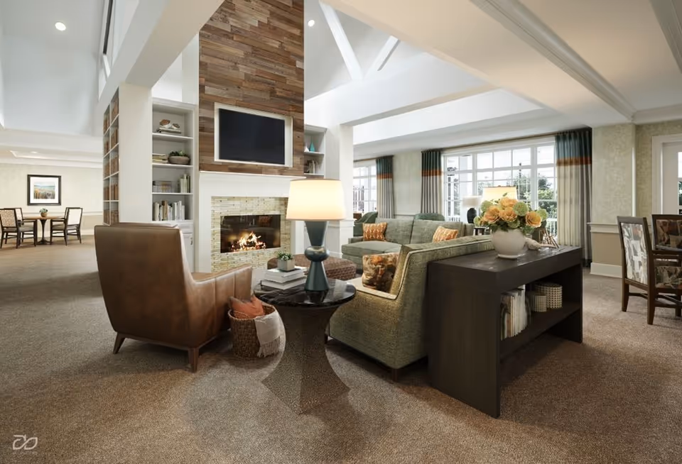 Spacious senior living lounge with sofas, an armchair, a fireplace and TV, and a dining area visible in the background.
