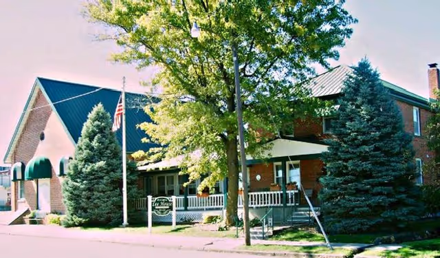 Front exterior of a brick senior living building with a covered porch, trees, a flagpole, and a small sign reading 'Lee House'.
