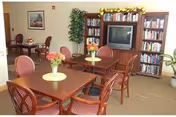 Interior common lounge at Hillside Woods I and II with tables, chairs, plants, and TV.