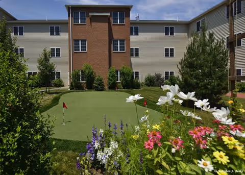 Multi-story senior living building with brick center and a colorful garden in foreground.