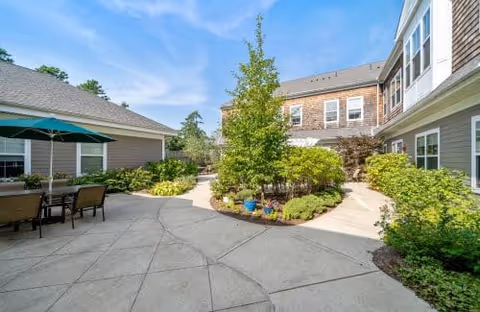 Sunny landscaped courtyard with paved walkways, patio seating, and surrounding residential buildings.