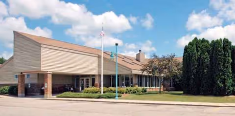 Exterior view of Wellington Meadows facility with a low-slung brick-and-siding building and landscaping.