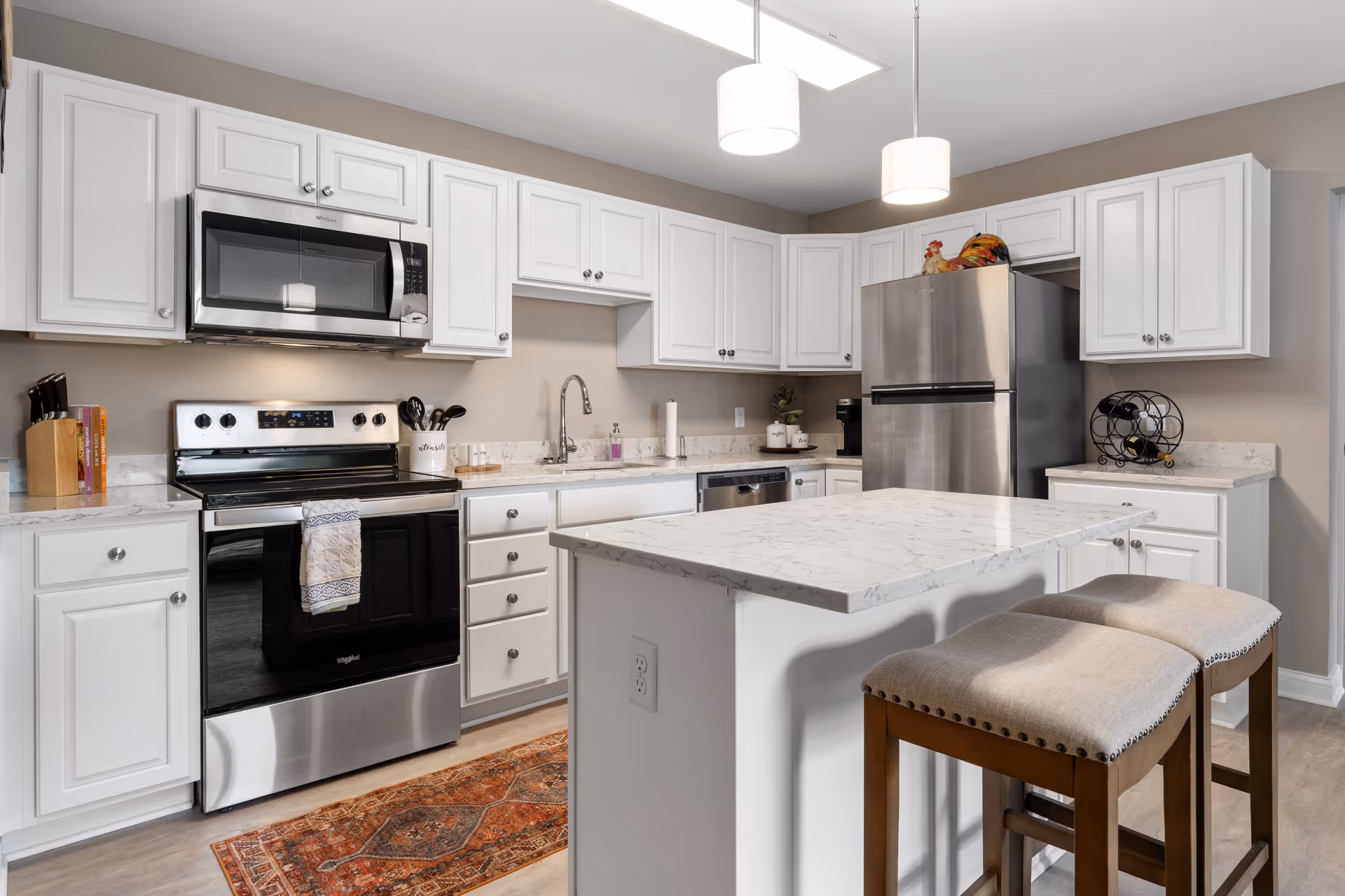 Bright modern kitchen with white cabinets, marble countertops, stainless steel appliances, and an island with two stools.