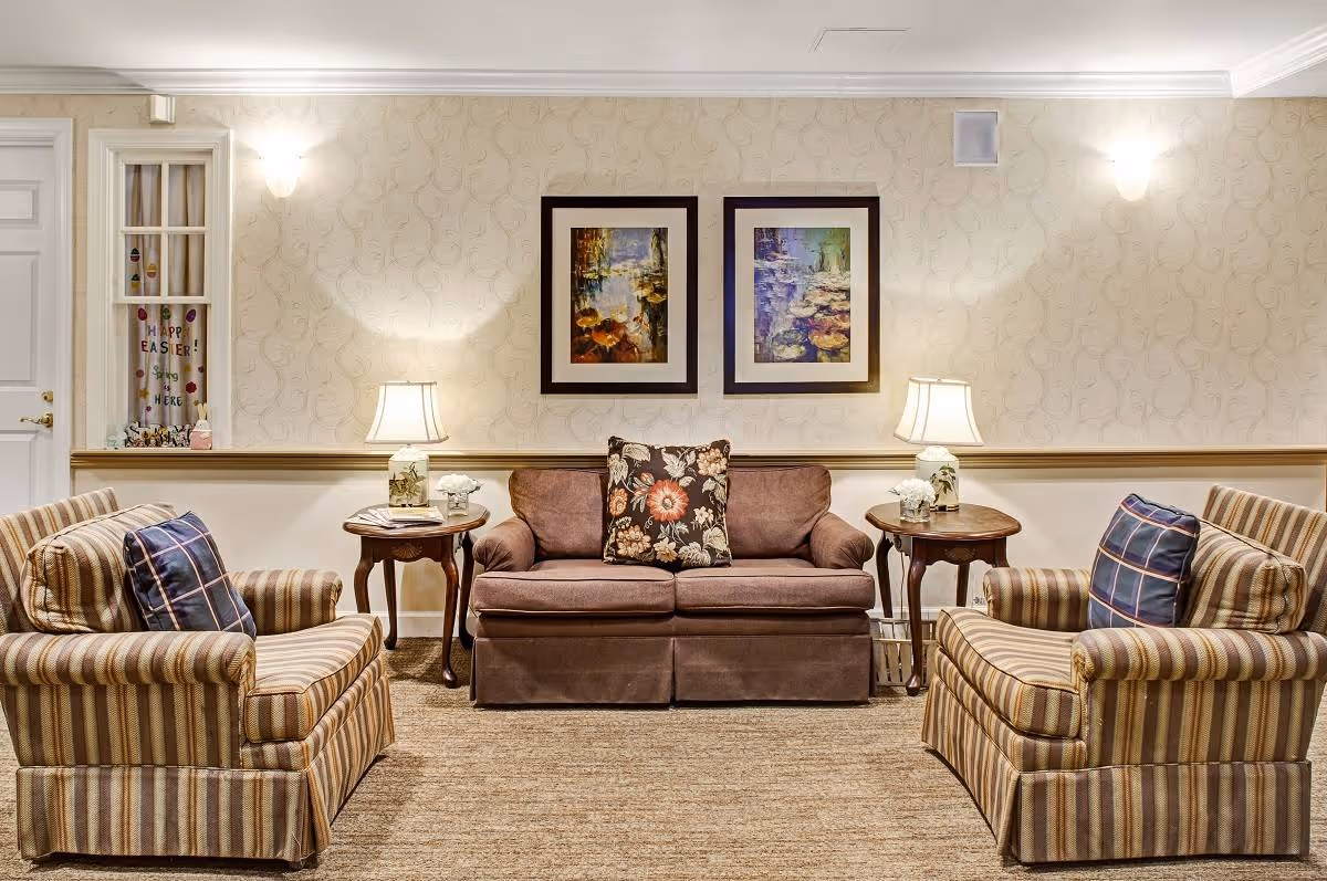 Cozy sitting area with a central sofa, two striped armchairs, side tables with lamps, and framed artwork on the wall.
