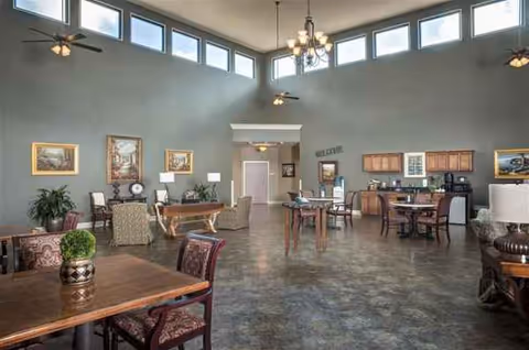 Spacious senior living common area with multiple seating groups, high windows, and a kitchenette.