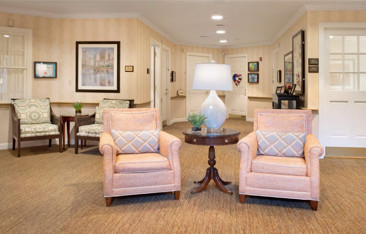 Lobby seating area with two peach armchairs flanking a round table with a lamp and additional chairs against the wall.
