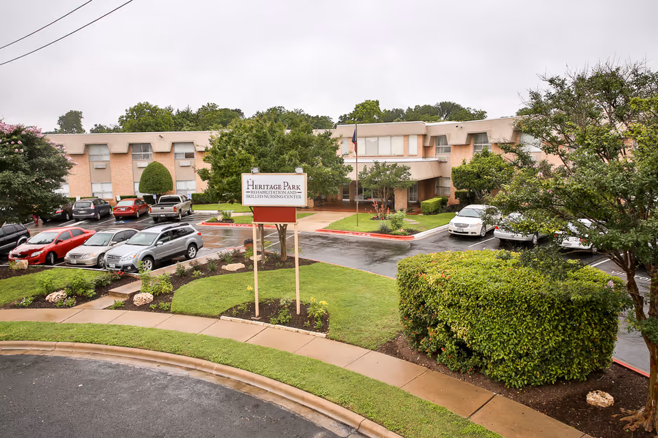 Front exterior of Heritage Park Rehabilitation and Skilled Nursing Center showing the entrance sign, parking lot, landscaped grounds, and the two-story building.