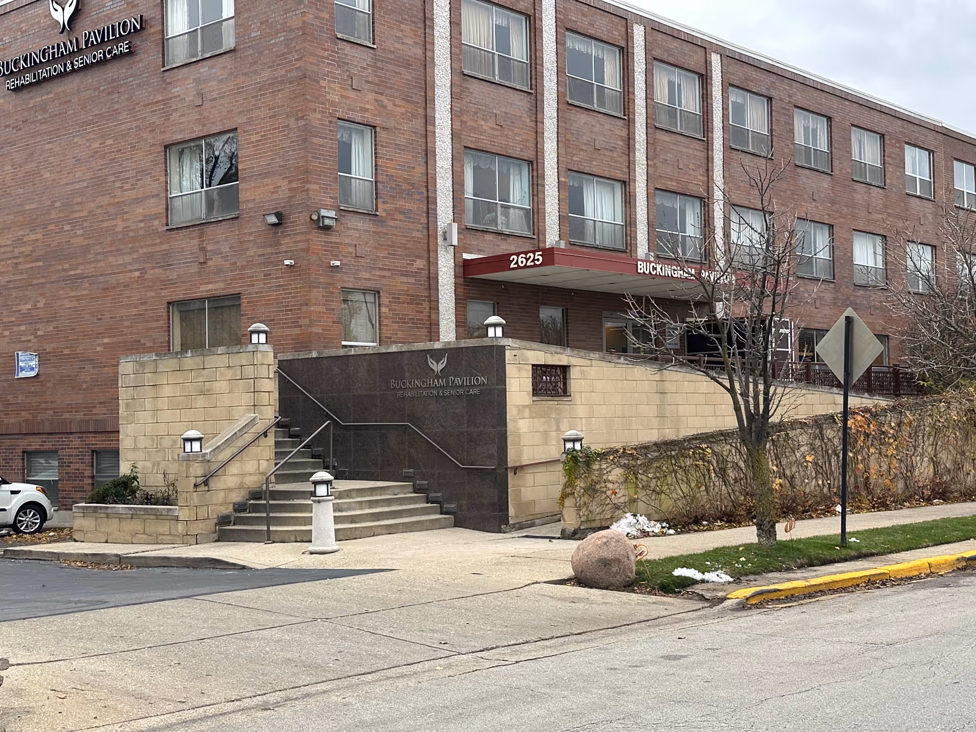 Exterior view of Buckingham Pavilion three-story brick nursing and rehabilitation building showing the main entrance, steps, and signage with address 2625.