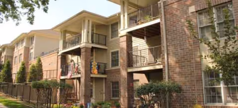 Exterior view of Charter Senior Living building with brick walls, balconies, and greenery.