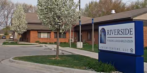 Exterior view of Riverside Nursing & Rehabilitation facility with sign and blooming trees