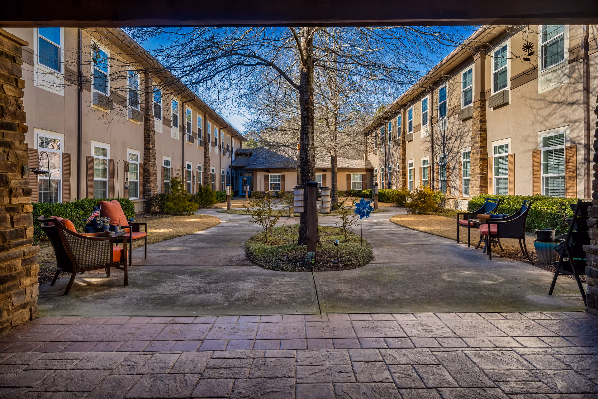 Central courtyard of a senior living facility with pathways, seating areas, and two-story building wings on either side.