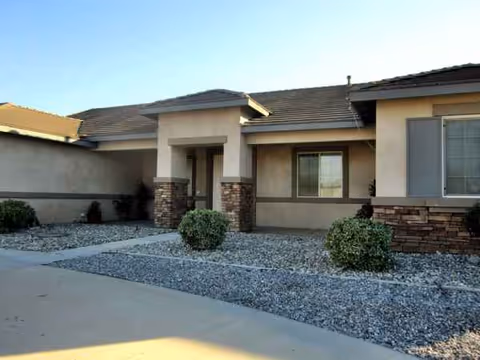 Single-story beige senior facility exterior with stone accents, gravel landscaping, and a driveway.