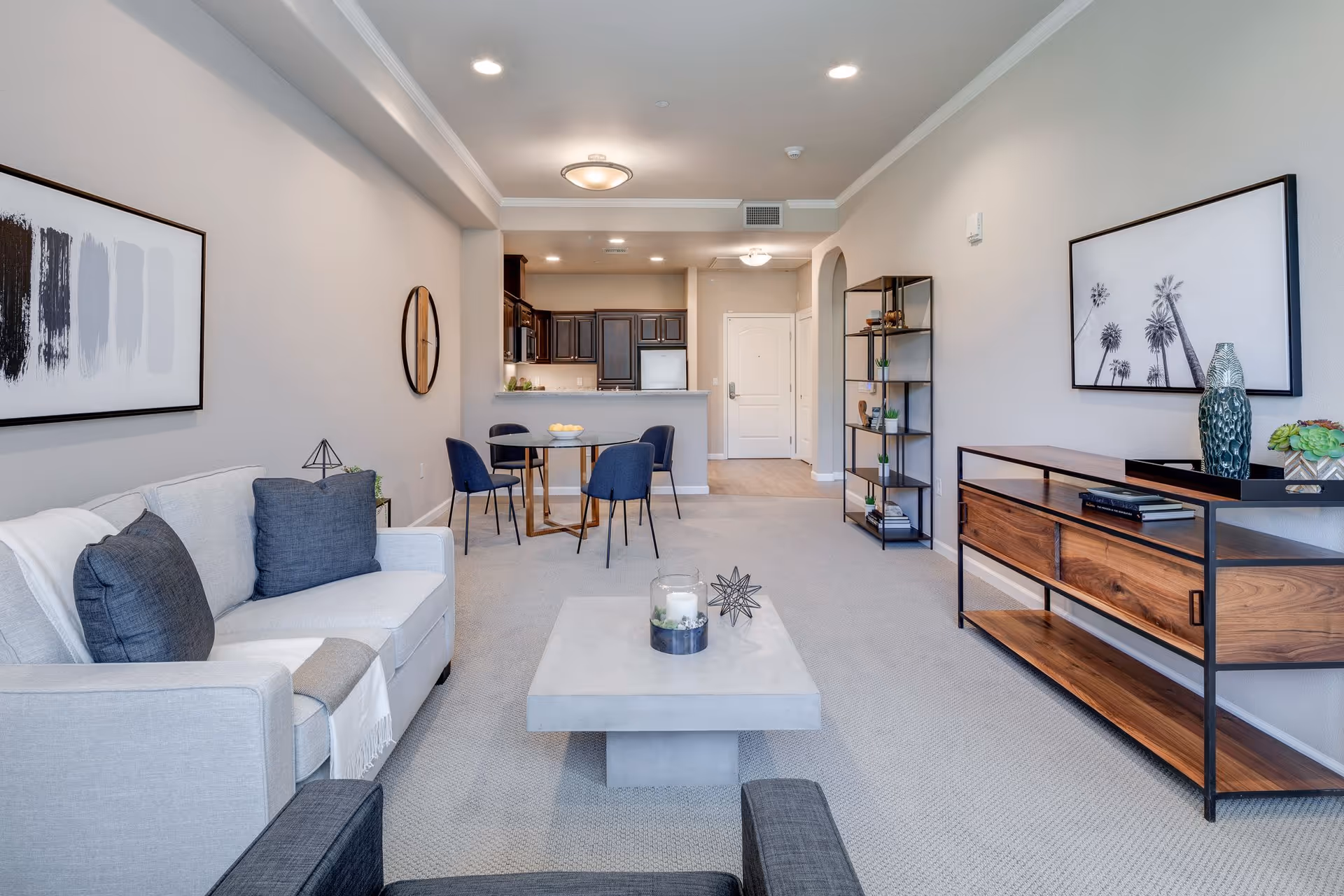 Open-plan living room with a light gray sofa, central coffee table, dining table and kitchen visible in the background.