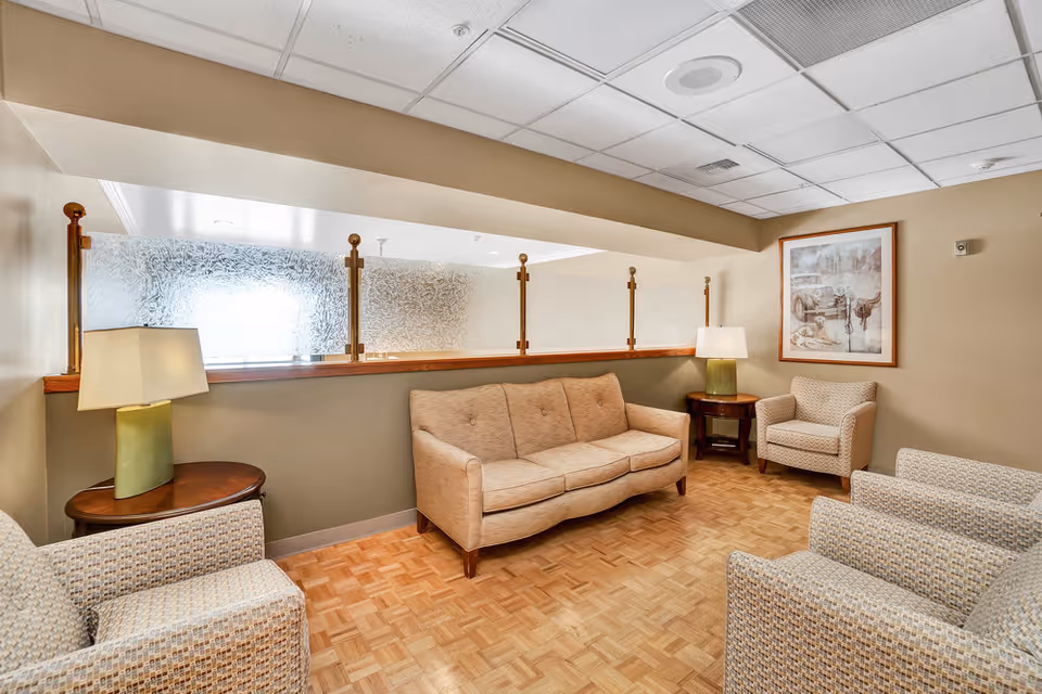 Cozy sitting area with a beige sofa, several armchairs, side tables with lamps, parquet flooring, and a frosted glass partition.