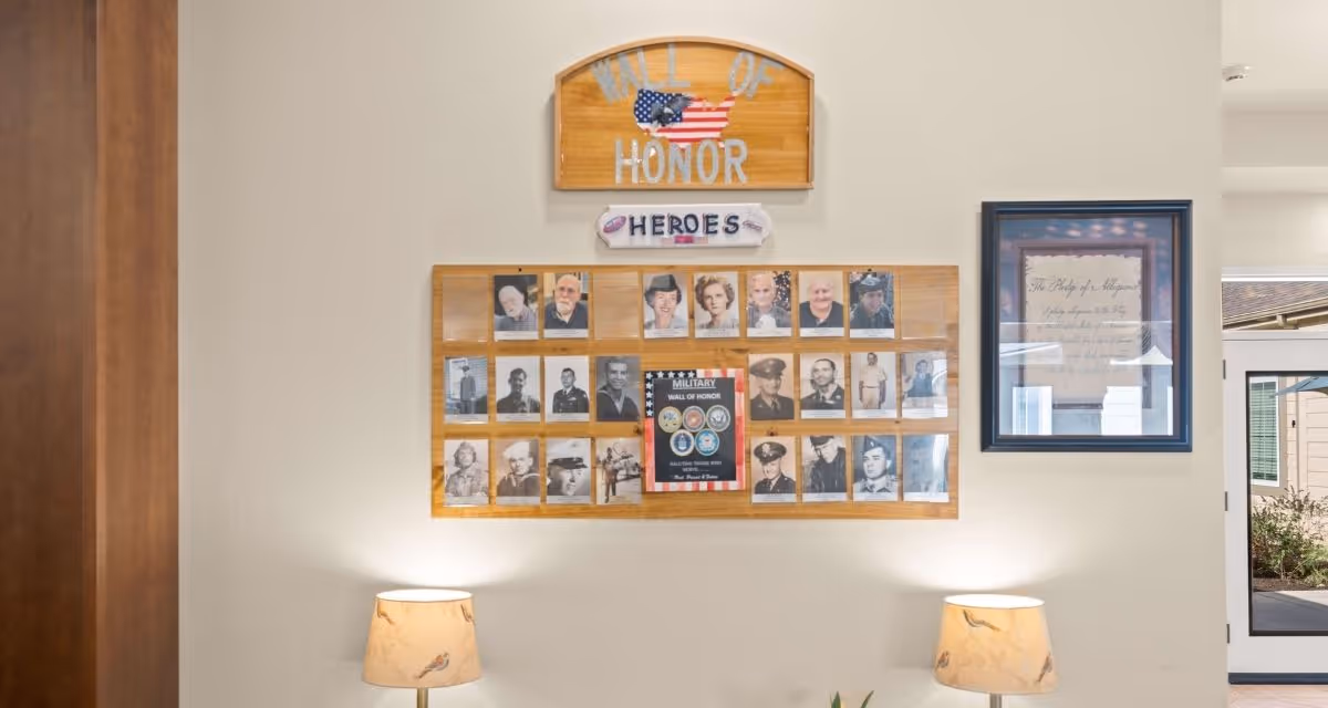Wall display titled 'Wall of Honor' featuring framed veterans' photos on an interior wall with two lamps below.