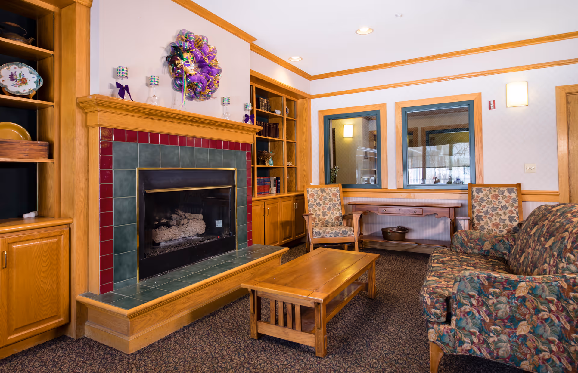 Cozy common living area with a tiled fireplace, built-in wooden shelving, upholstered seating, and a wooden coffee table.
