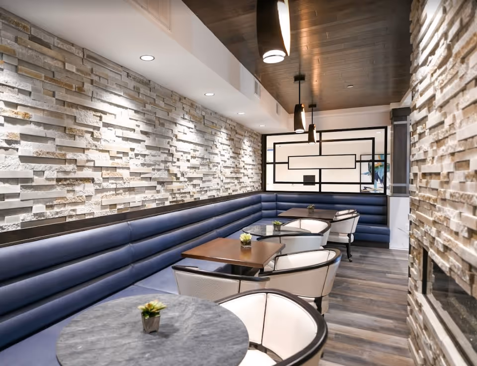 Modern dining lounge with a long blue banquette, round and square tables, white chairs, stone accent walls and pendant lights.