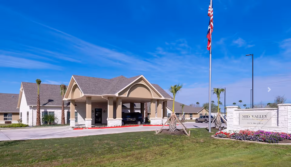 Front entrance of Mid Valley Nursing & Rehabilitation with a porte-cochere, flagpole, landscaped lawn and a stone sign.