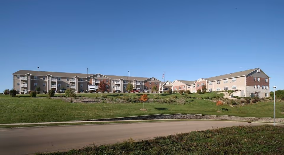 A long multi-story senior living facility building on a grassy hill under a clear blue sky.