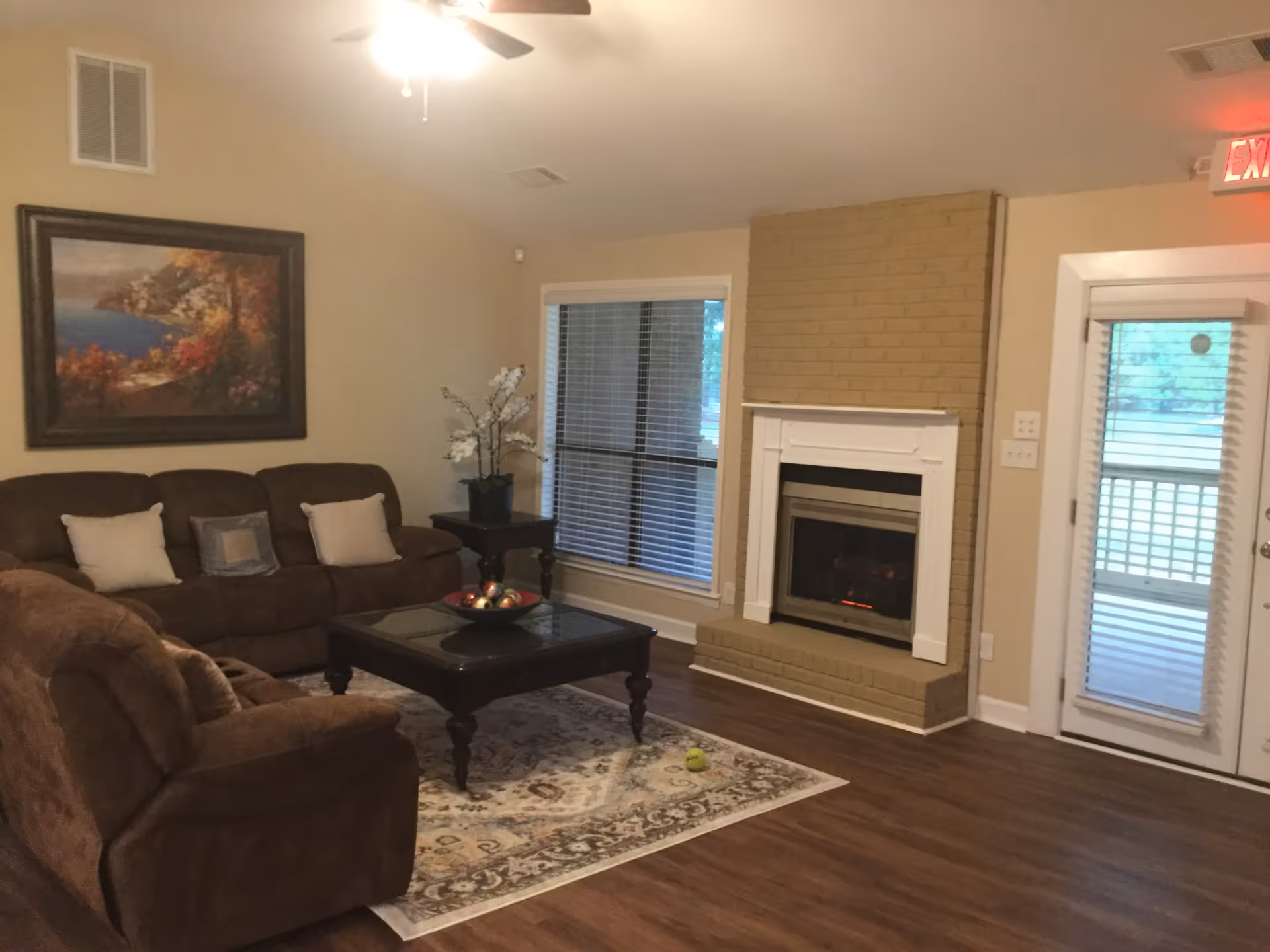 Cozy living room with brown sofas, a coffee table on a rug, a fireplace, framed artwork, and a glass door.