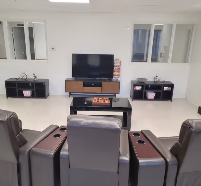 Leather recliners facing a flat-screen TV on a media console with a coffee table in a bright common room.