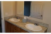Double-sink bathroom vanity with granite countertop, wooden cabinets and a large wall mirror.