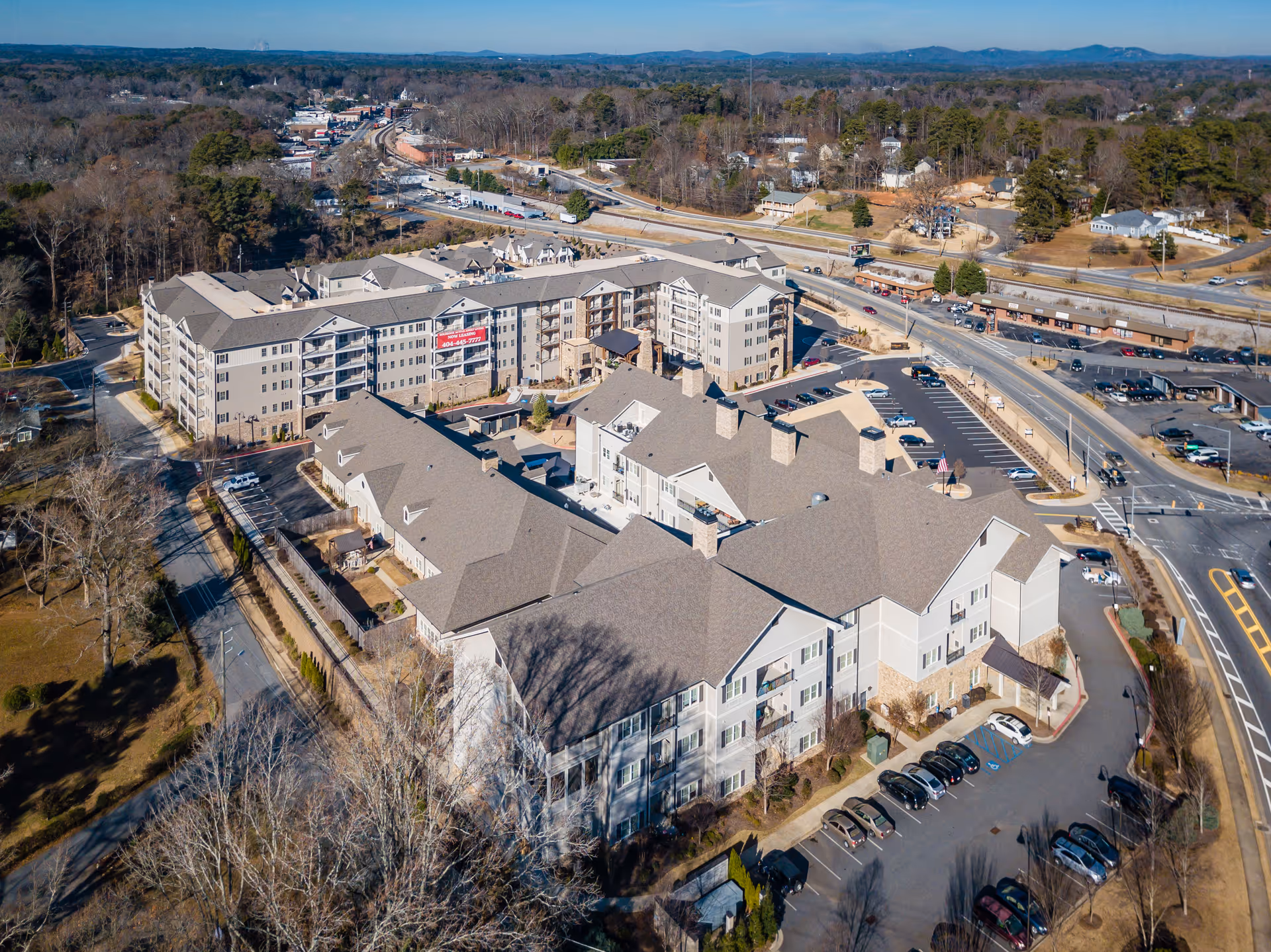 Aerial view of a large senior living facility complex named Holbrook Acworth, showing multiple connected buildings with parking lots, surrounding roads, and nearby trees and residential areas under a clear blue sky.