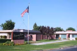 Delano PostAcute Care building with flagpole, manicured lawn, and trees.