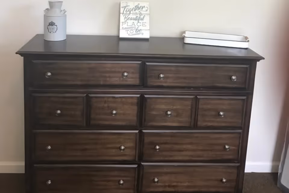 Dark wooden dresser with multiple drawers topped with decorative items against a light wall.