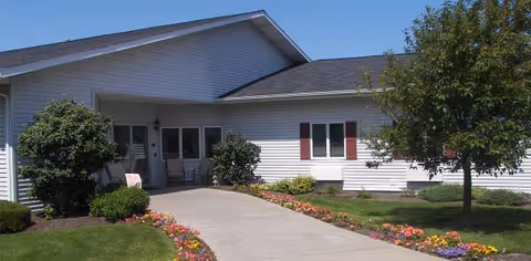 Single-story senior living facility exterior with a curved walkway and colorful flower beds.
