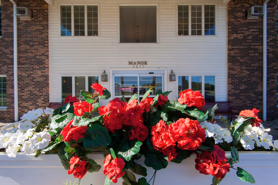 Front entrance of a manor building with a planter of red and white flowers in the foreground.