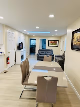 Dining table with chairs in an open-plan living area featuring sofas and wall art.