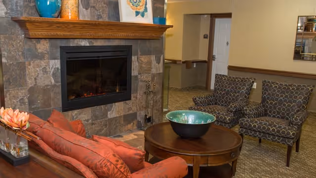 Cozy lounge area with a stone fireplace, a red sofa, two patterned chairs, and a round coffee table with a decorative bowl.