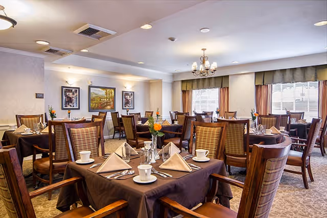 Dining room with multiple tables set with folded napkins, cups, silverware and small floral centerpieces.