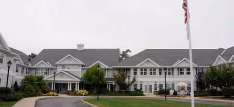 Sunrise of Plymouth Beach exterior building with parking and landscaping.